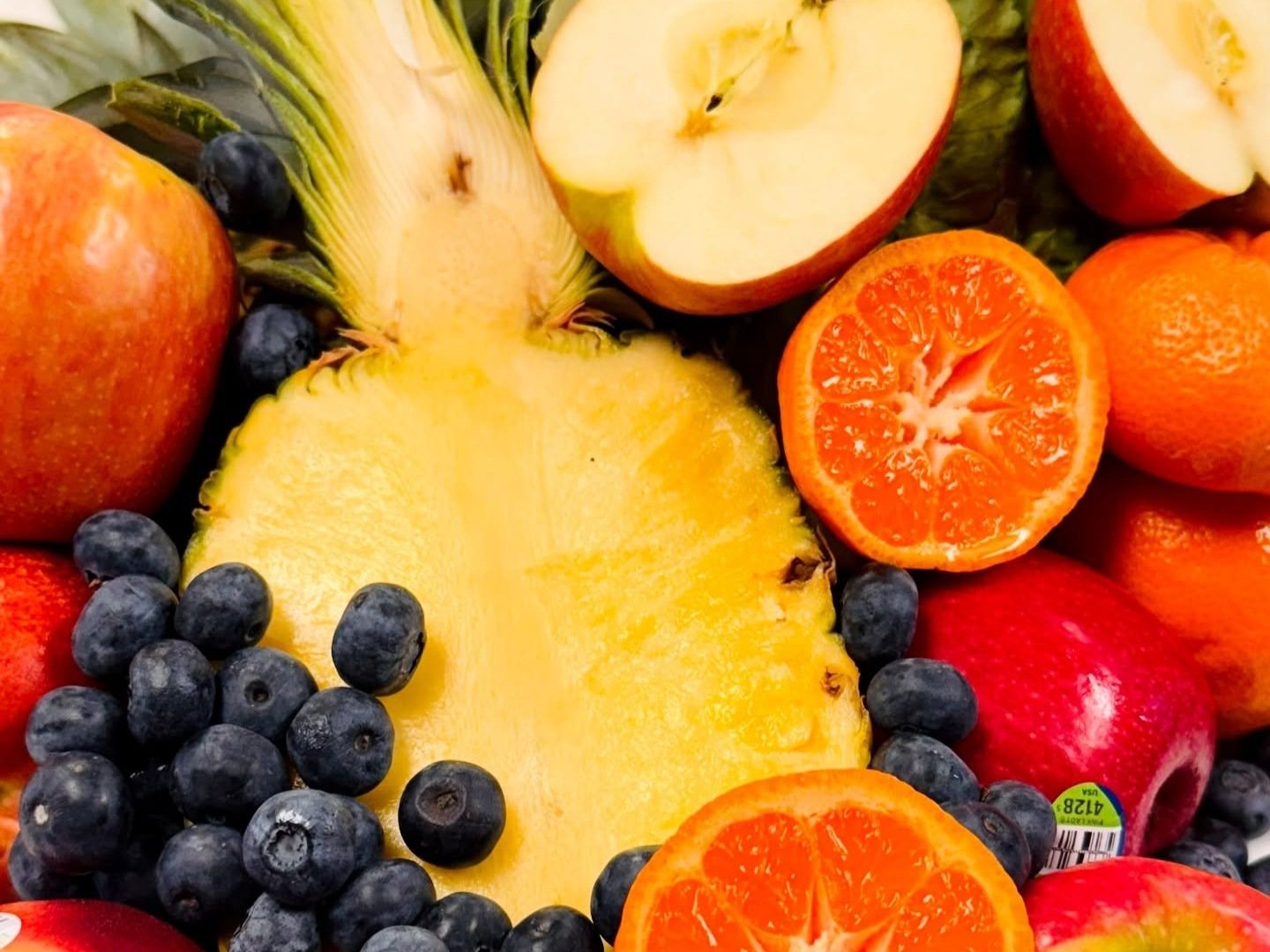 Vibrant assortment of fresh fruits including red apples, blueberries, pineapple, and oranges arranged artfully, showcasing a colorful and healthy selection.