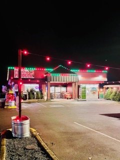 Brightly lit convenience store decorated with festive red and green lights at night, showcasing a welcoming atmosphere. The parking lot is empty, and holiday decorations enhance the store's appeal.