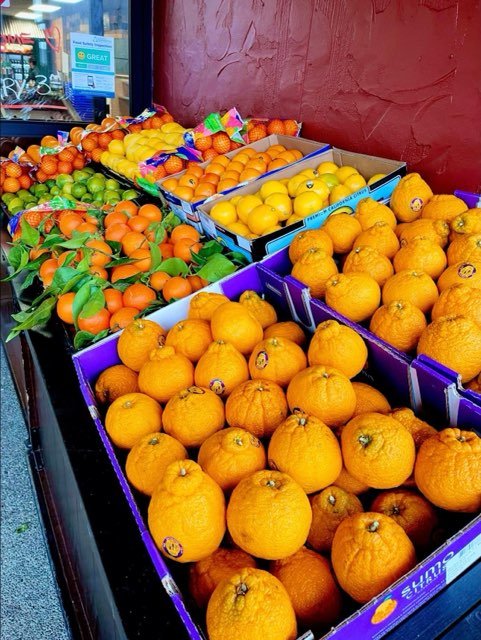Vibrant display of fresh oranges, tangerines, and citrus fruits at a local market, showcasing a colorful assortment in wooden crates against a textured wall backdrop.